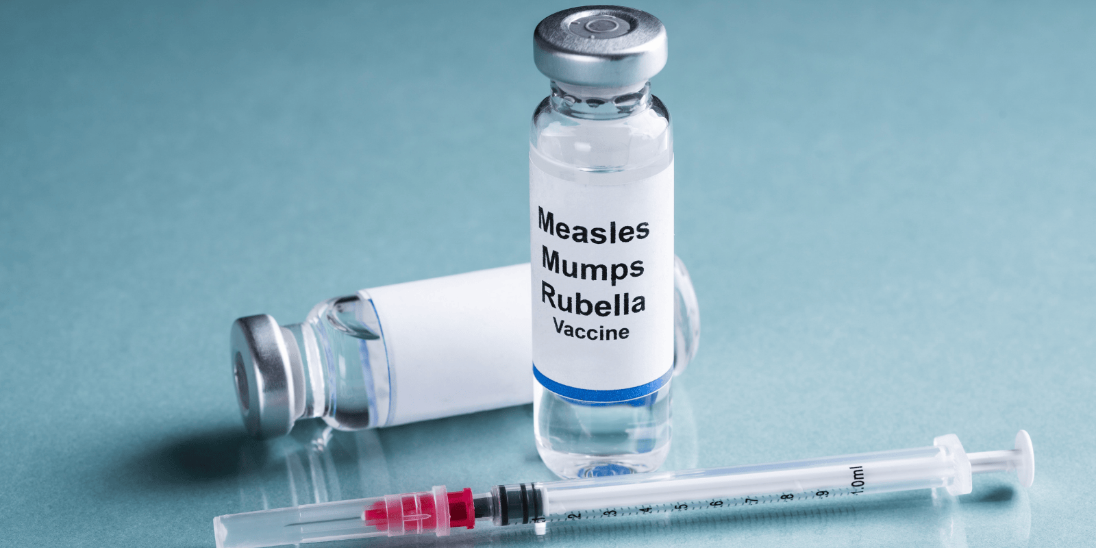 Two vials of the measles, mumps, rubella (MMR) vaccine next to a needle syringe.