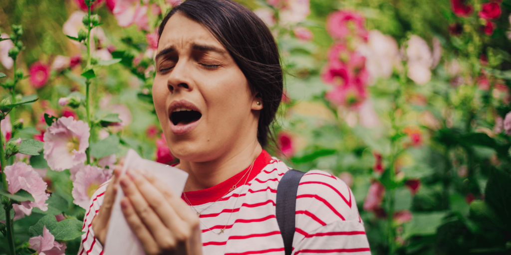 A woman surrounded by flowers sneezing into a tissue