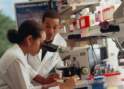 A scientist sitting at a lab bench looking through a microscope