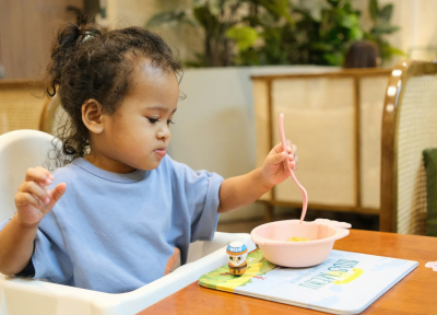 A toddler in a highchair eating from a bowl
